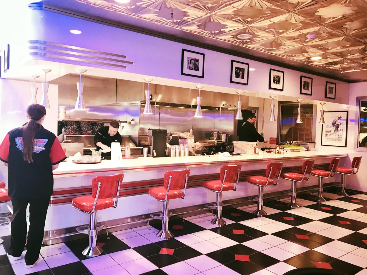 A retro-style diner with red bar stools and a classic checkered floor.