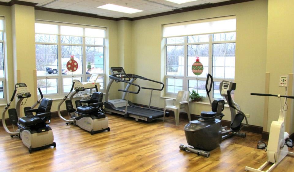 A well-lit gym with exercise equipment including a treadmill and stationary bikes.