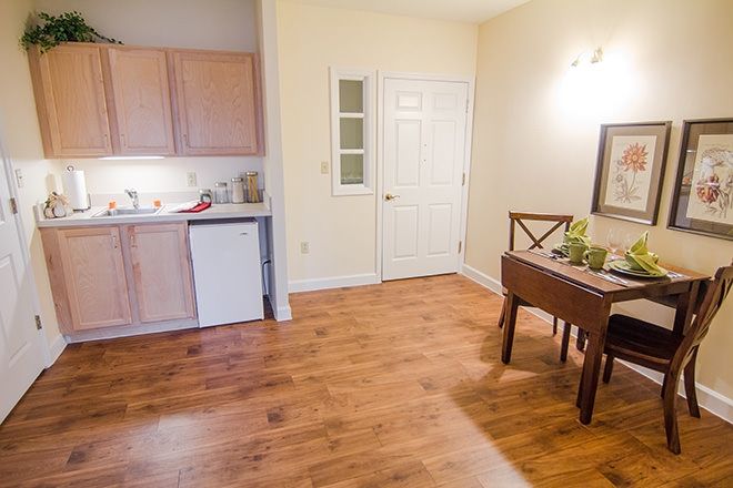 A cozy kitchen and dining area with hardwood floors, featuring a small set of cabinets, a compact fridge, and a dining table with chairs.