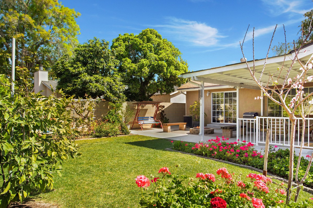 A serene backyard with a lush green lawn, vibrant flowers, and a cozy patio area.