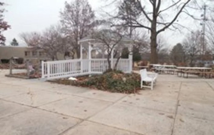 A white gazebo surrounded by bare trees and a bench in a winter landscape.