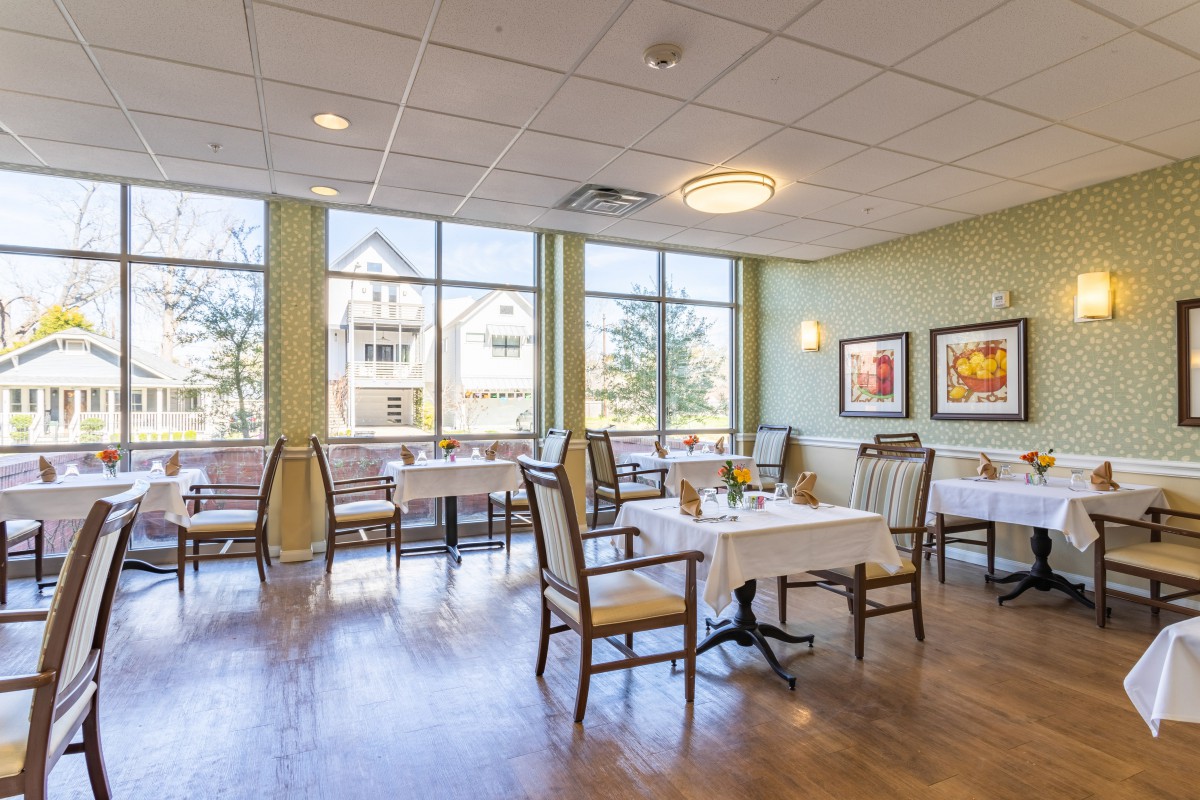 A bright and inviting dining area with neatly arranged tables and chairs, large windows, and decorative artwork on the walls.