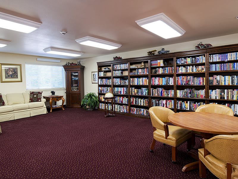 A cozy library room with bookshelves, comfortable seating, and a table for reading or study.