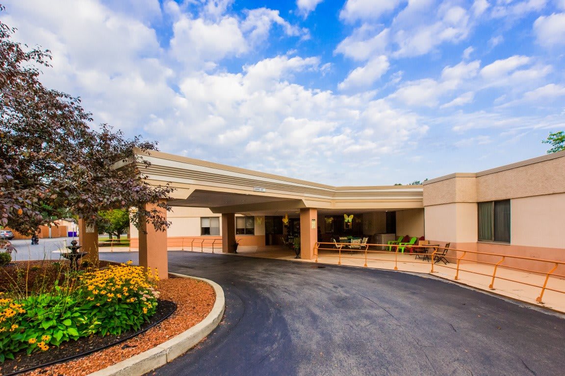 A building entrance with a circular driveway and landscaped surroundings under a cloudy sky.