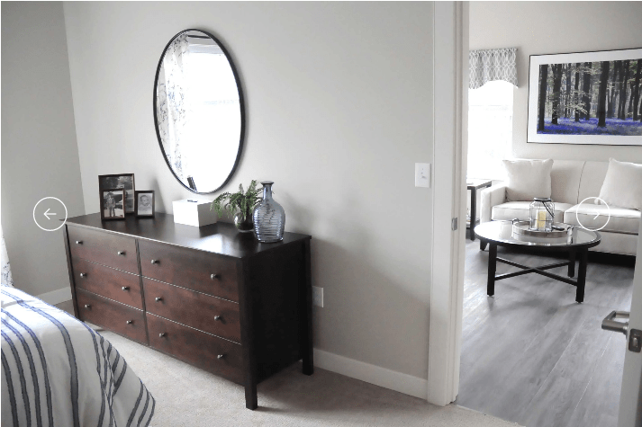 A modern bedroom with a dark wooden dresser and a round mirror on the wall.