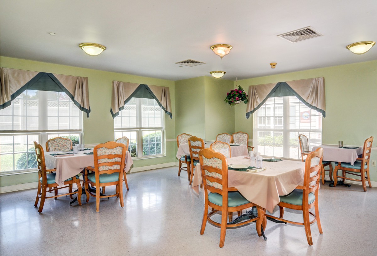 A cozy dining area with tables and chairs, adorned with large windows and curtains.