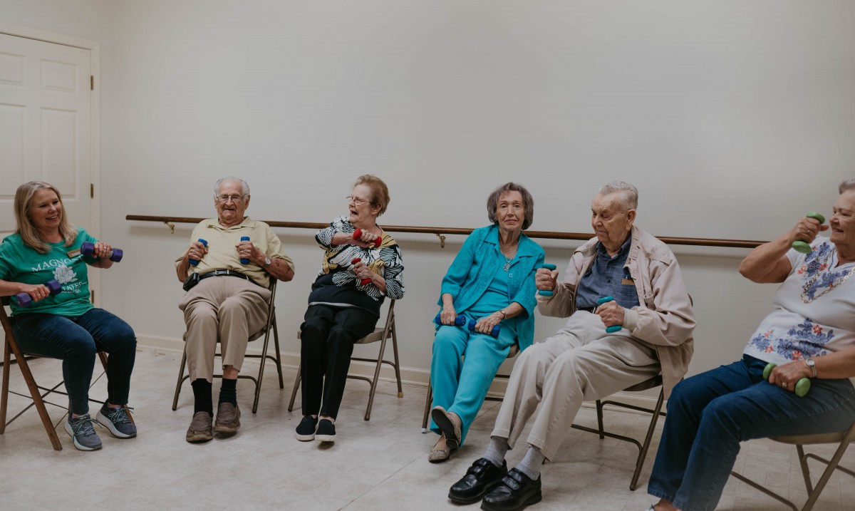 A group of elderly people sitting on chairs, engaging in a community activity indoors.