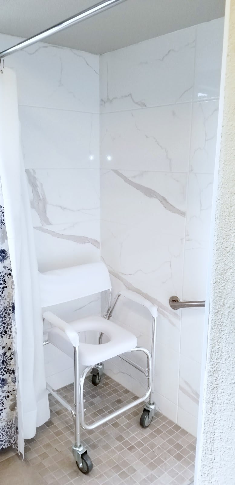 A shower area featuring a white shower chair and marble walls, designed for accessibility.