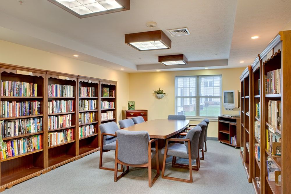 A cozy library meeting room with bookshelves, a table, and chairs by a window.
