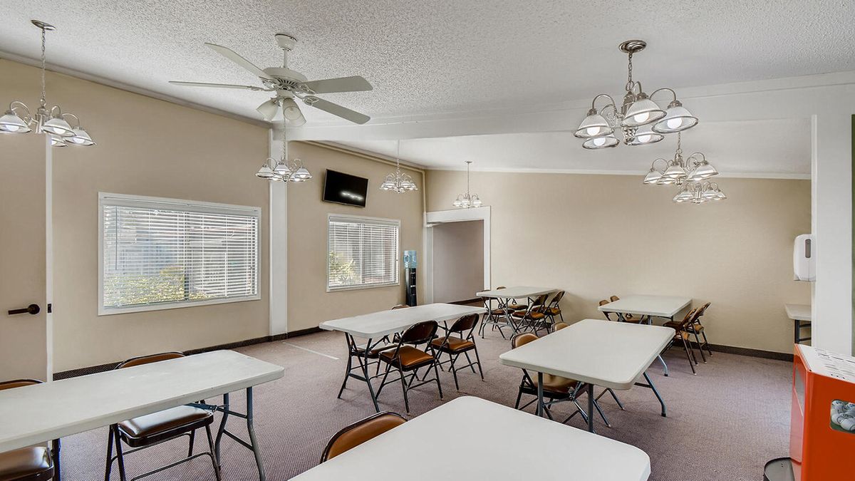 A spacious meeting room with multiple tables and chairs, featuring ceiling fans and chandeliers.