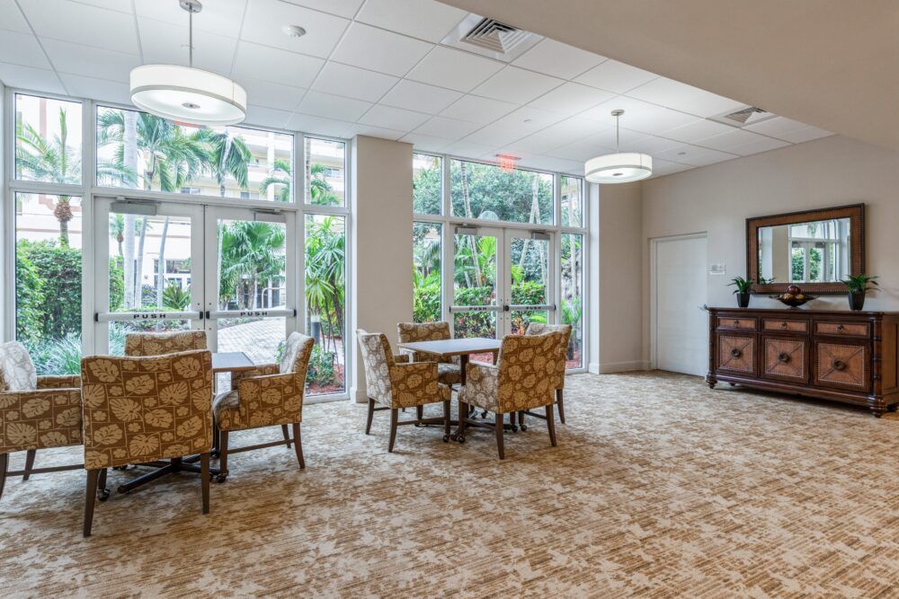 A spacious lounge with tables and chairs, featuring large windows that let in natural light.