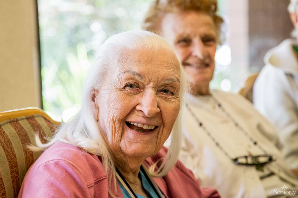 Two elderly women smiling and enjoying time together indoors.