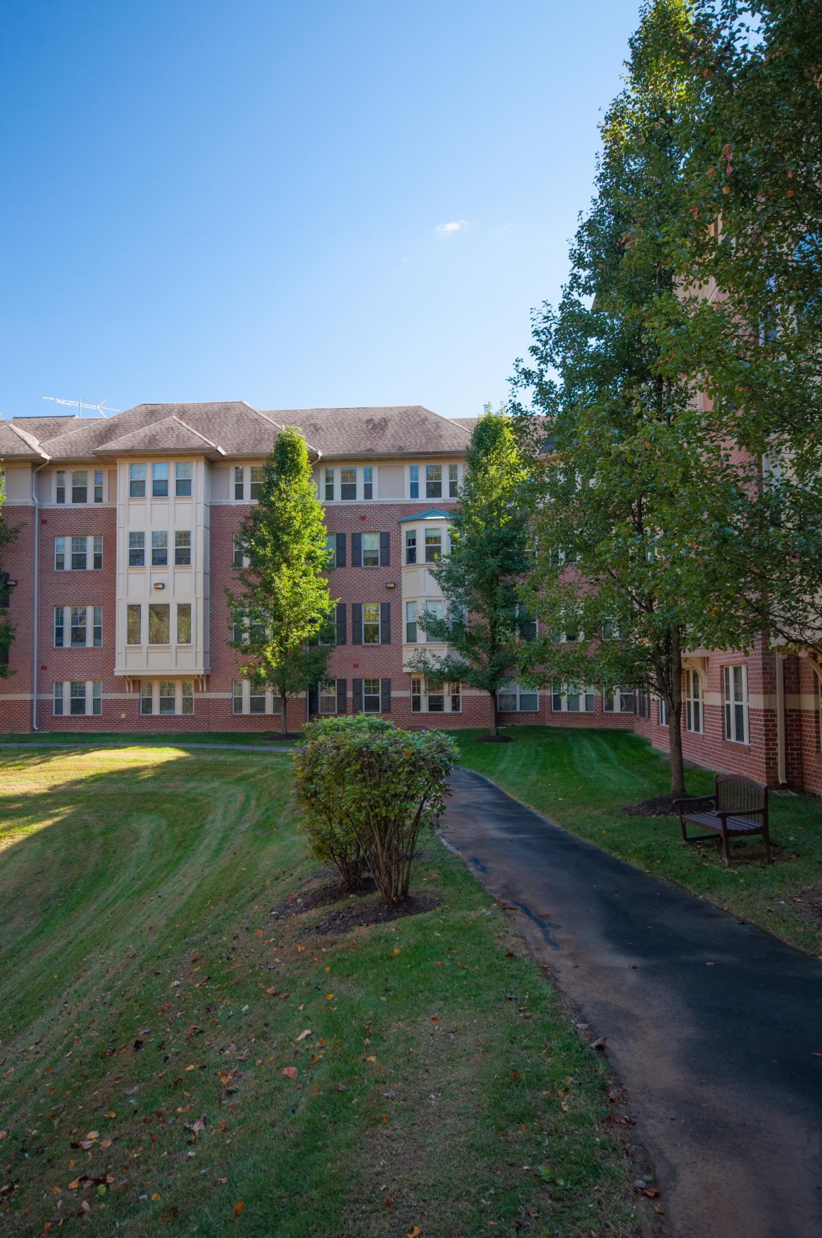 A brick residential building with a landscaped pathway and lush greenery.