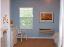 A cozy bedroom with blue walls, featuring a window with blinds, a dresser, a chair, and a framed painting on the wall.