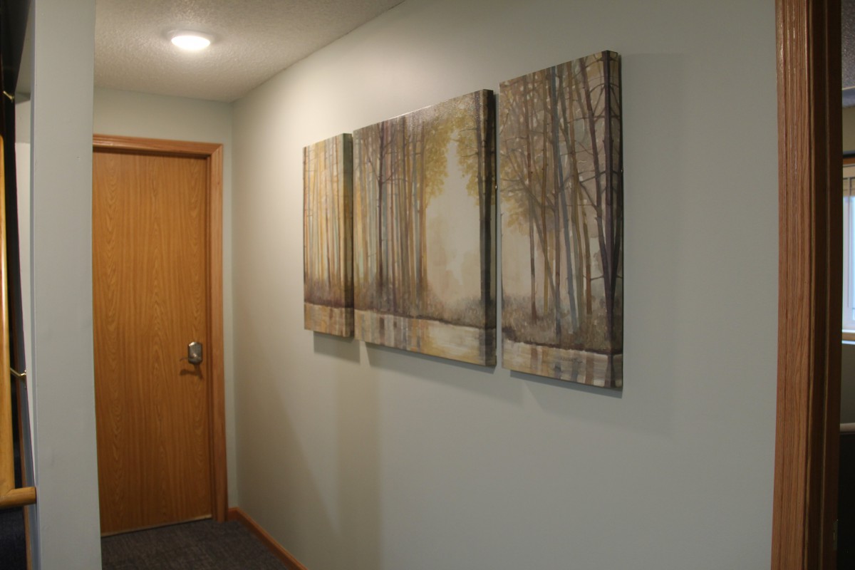 A hallway featuring a triptych of abstract tree paintings mounted on the wall.