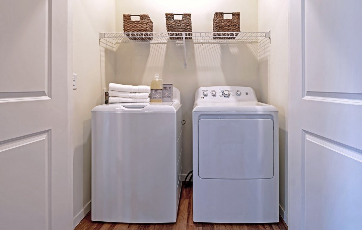 A tidy laundry room with a washer and dryer, featuring shelves with baskets and neatly folded towels.