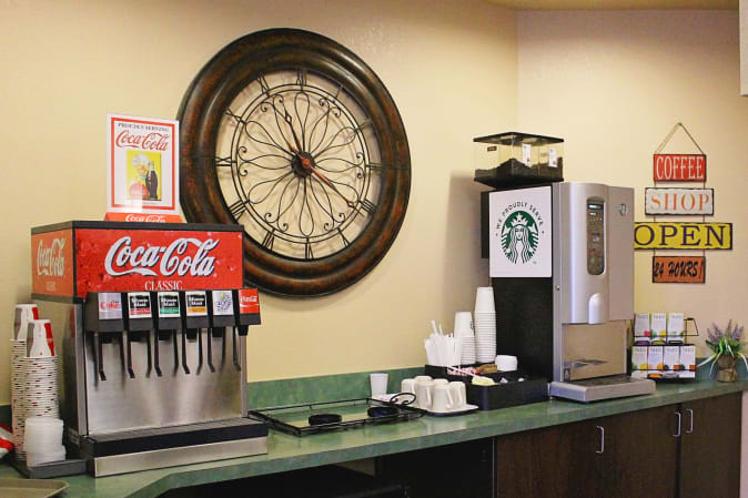 A beverage station featuring Coca-Cola drink dispensers and a Starbucks coffee machine, accompanied by a large decorative clock on the wall.
