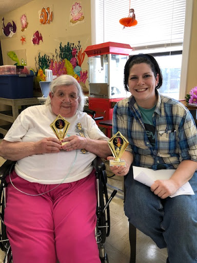 A joyful moment shared between a caregiver and an elderly resident, both proudly holding their trophies.