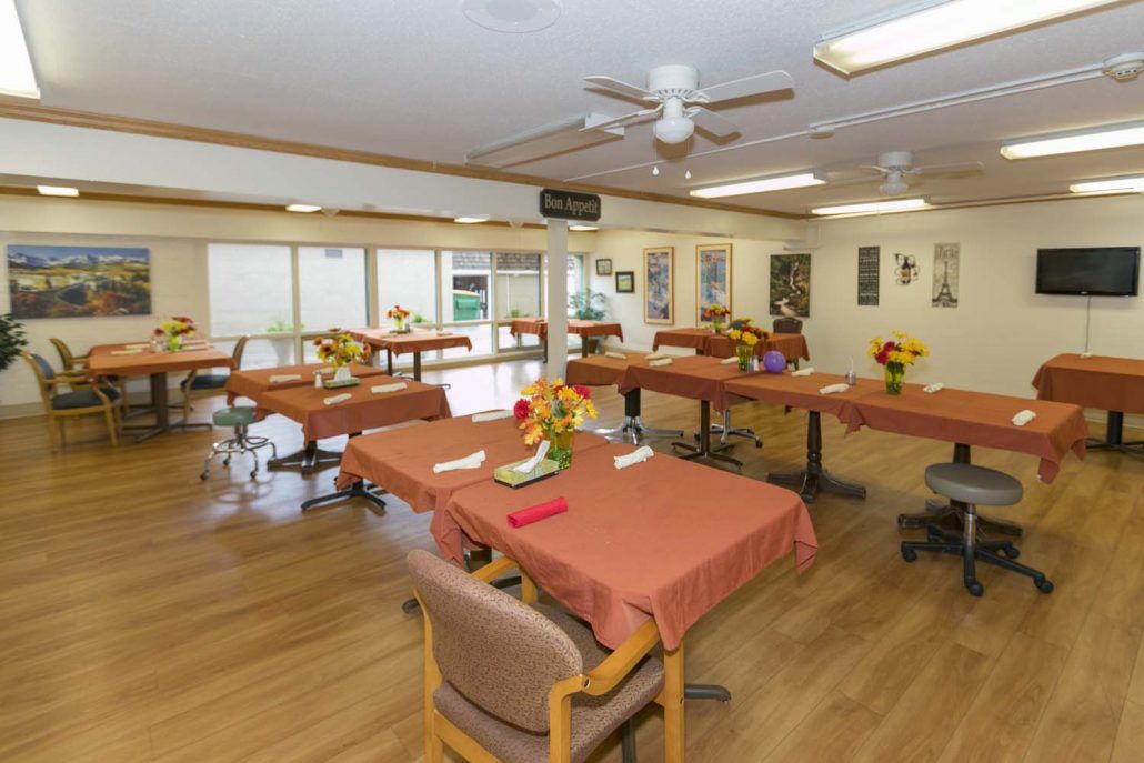 A spacious dining hall with neatly arranged tables and chairs, adorned with flower arrangements.