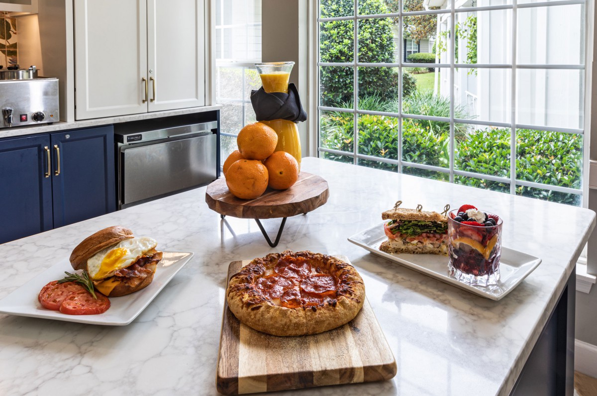 A breakfast spread featuring pizza, sandwiches, fresh oranges, and orange juice on a kitchen countertop.