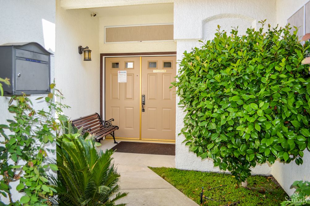 A welcoming house entrance with a bench and lush greenery.