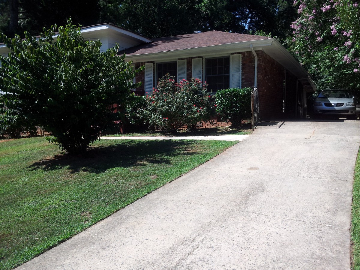 A small brick house with a driveway and a neatly maintained front yard.