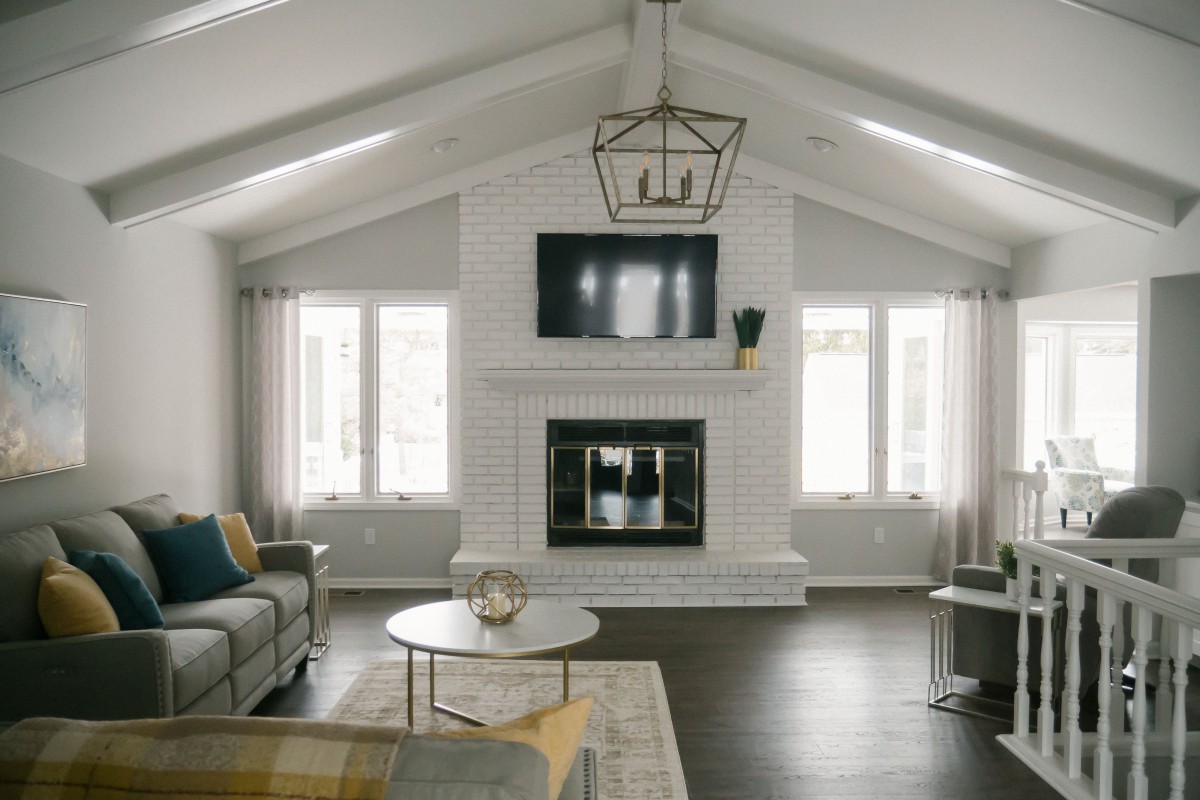 A modern living room with a minimalist design, featuring a central fireplace and overhead TV, flanked by large windows.