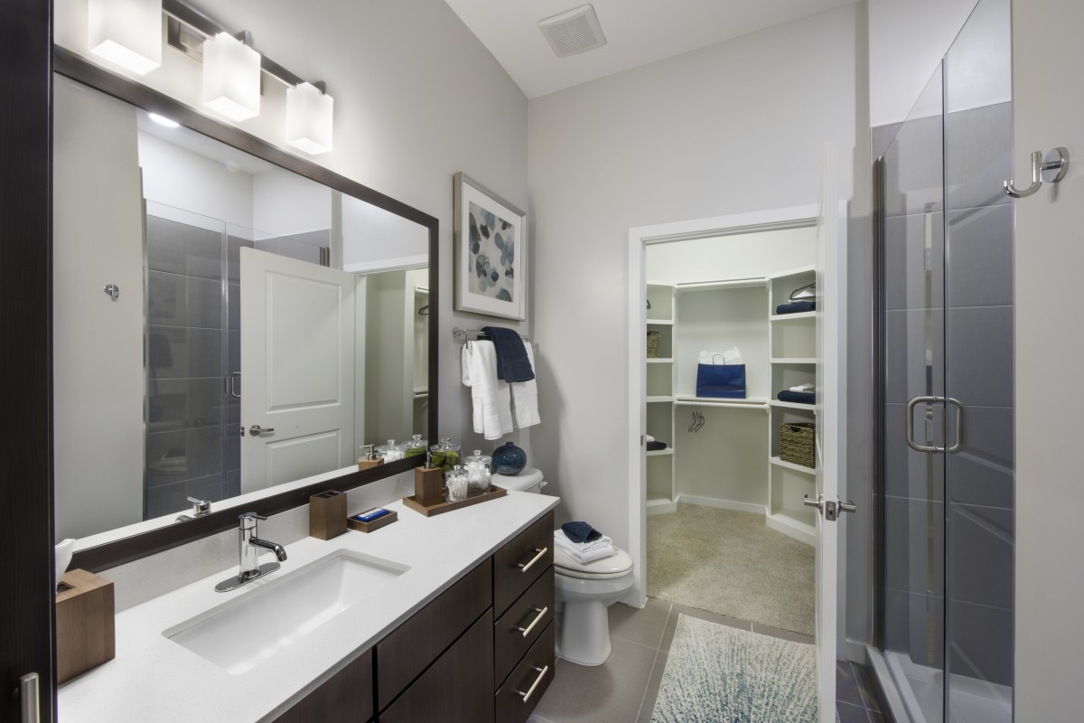 A modern bathroom with a large mirror, countertop sink, and neatly organized shelves in the background.