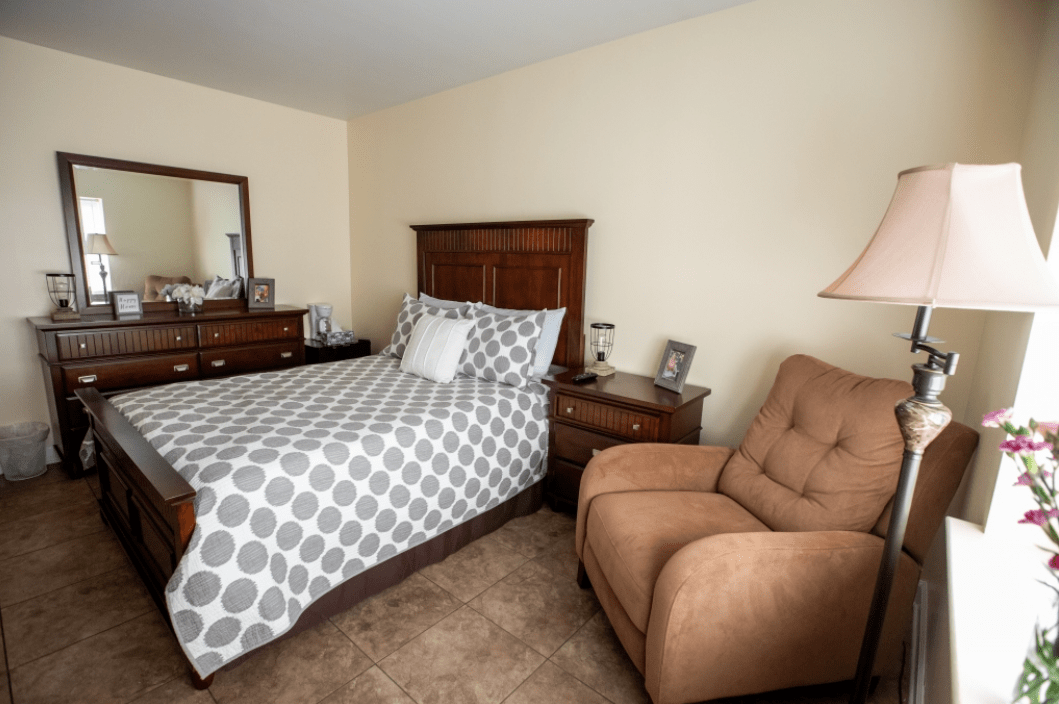 Cozy bedroom with a bed, dresser, armchair, and lamp.