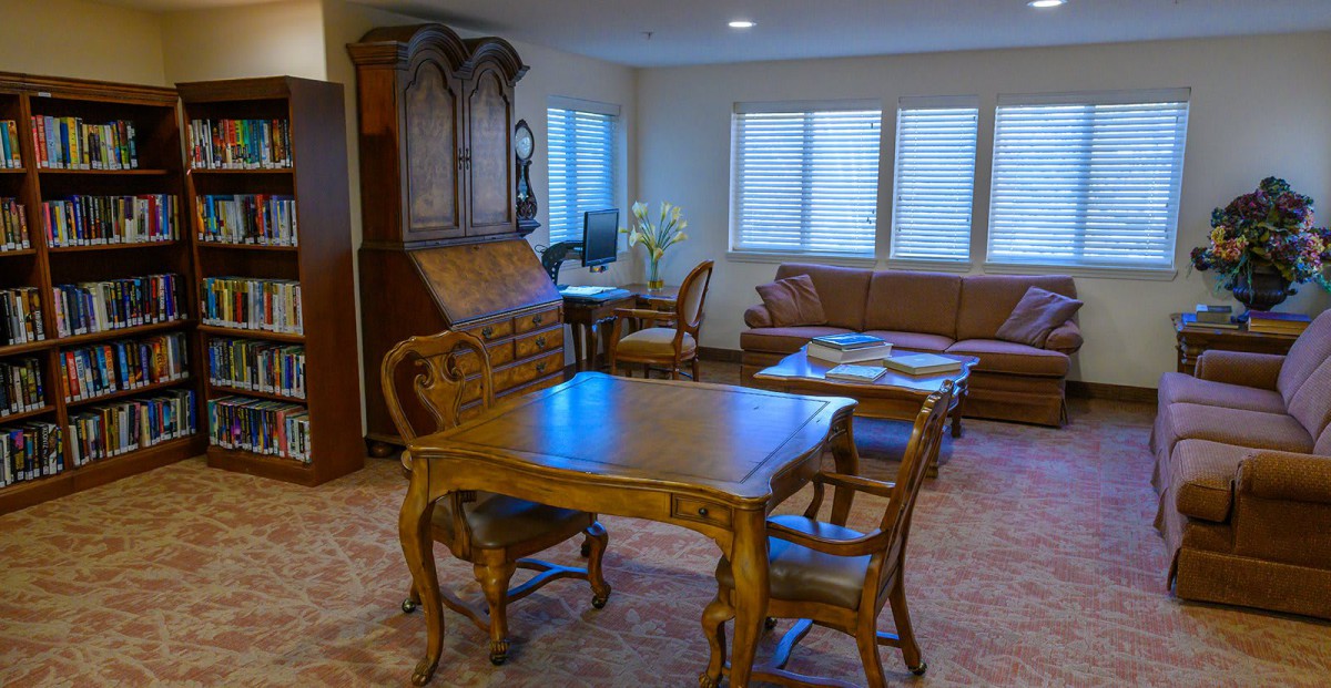 A cozy living room featuring classic wooden furniture and a comfortable sofa with ample lighting from windows.