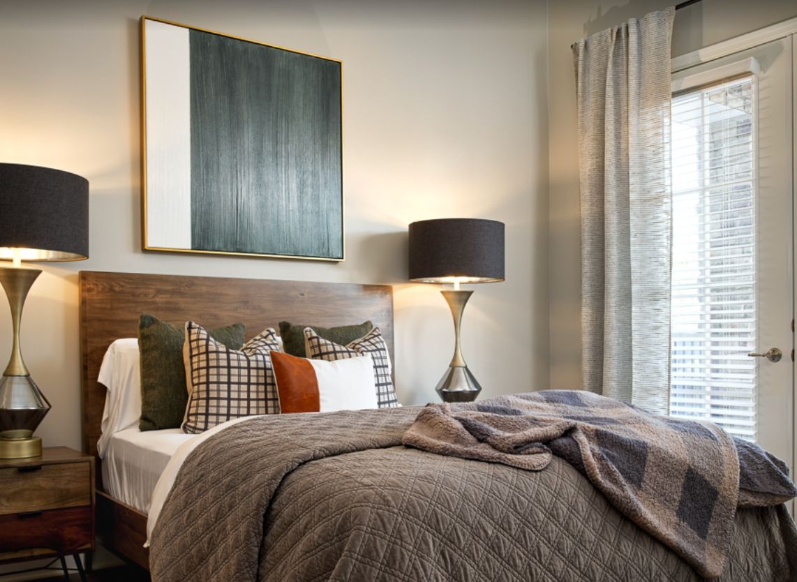 A modern and cozy bedroom with stylish decor, featuring a neatly made bed adorned with various pillows, a lamp on the side, and contemporary artwork on the wall.