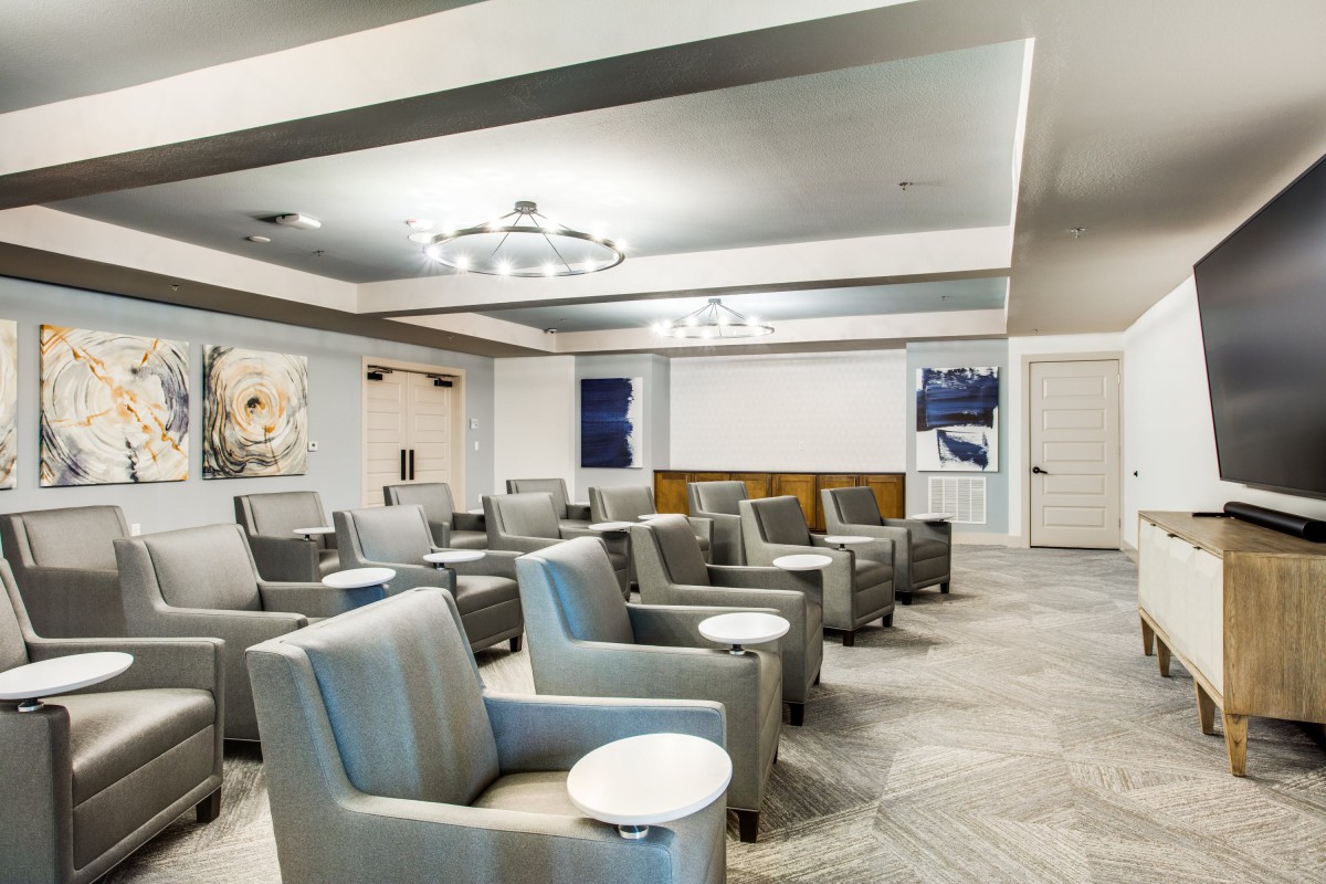 A modern conference room with gray armchairs and round side tables, featuring contemporary artwork on the walls.
