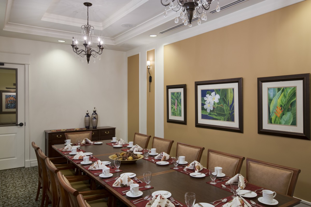 A formal dining room with a long table set for a meal, featuring elegant chandeliers and framed artwork on the walls.