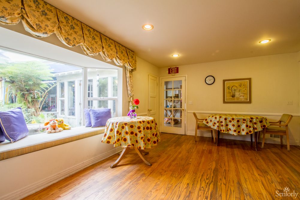 A cozy dining room with a window seat and bright natural lighting, featuring wooden flooring and floral decor.