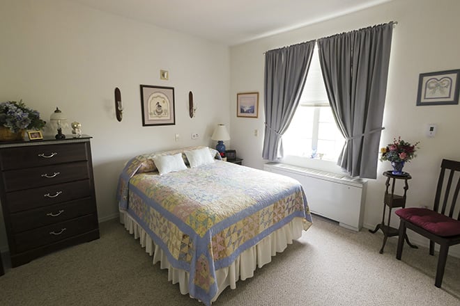 A cozy bedroom with a neatly made bed, wall art, and large windows with curtains.