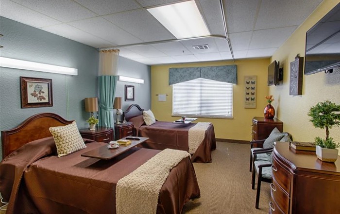 A well-arranged hospital room featuring two patient beds with bedside tables and comfortable seating.