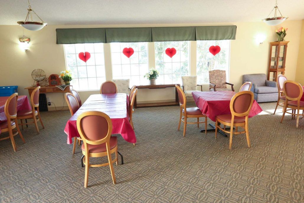 A cozy dining area with tables covered in red tablecloths and heart-shaped decorations on the windows.
