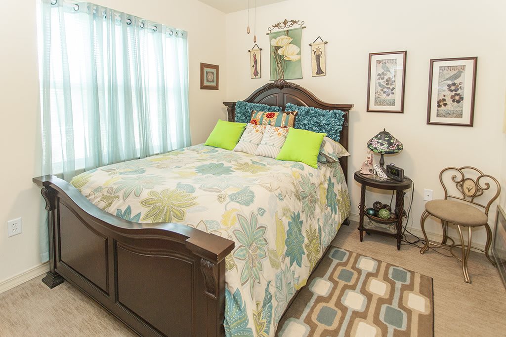 A cozy bedroom featuring a wooden bed with a colorful quilt and pillows, accompanied by a nightstand and decorative elements.