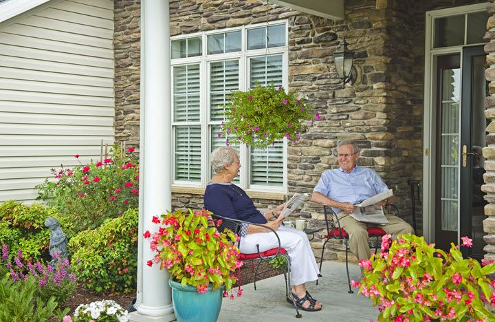 Two seniors enjoying a conversation on a porch surrounded by flowers.