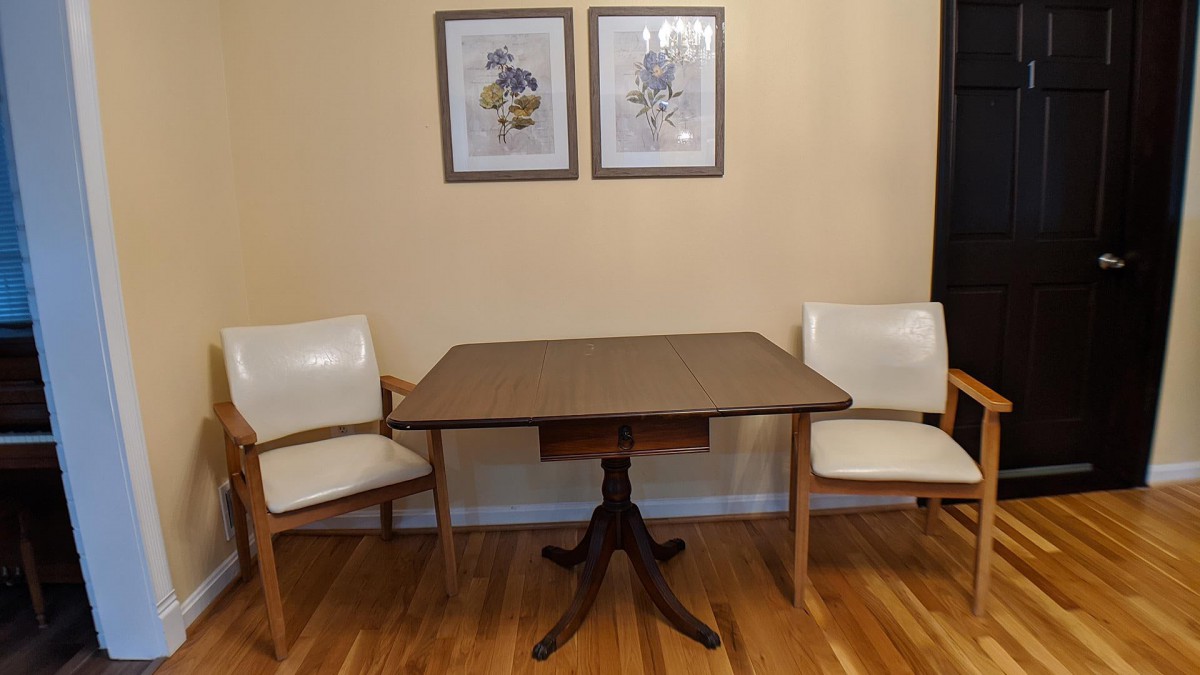 A cozy dining area featuring a wooden dining table with two white chairs and framed artwork on the wall.