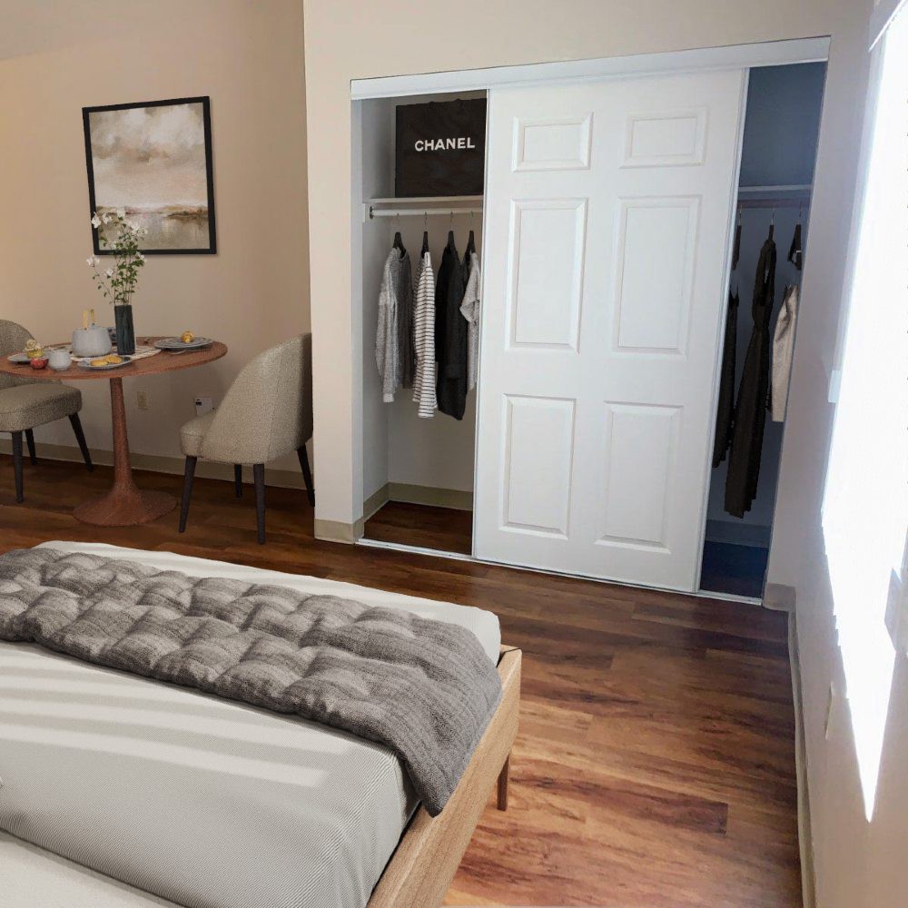 A modern bedroom with a neatly arranged bed, sliding closet doors, and a desk in the corner.