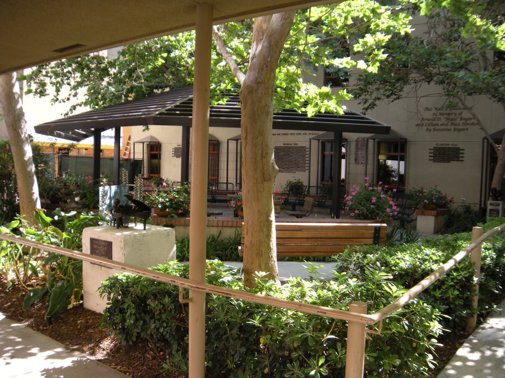 A tranquil courtyard featuring a tree, outdoor seating, and a sculpture surrounded by lush greenery.