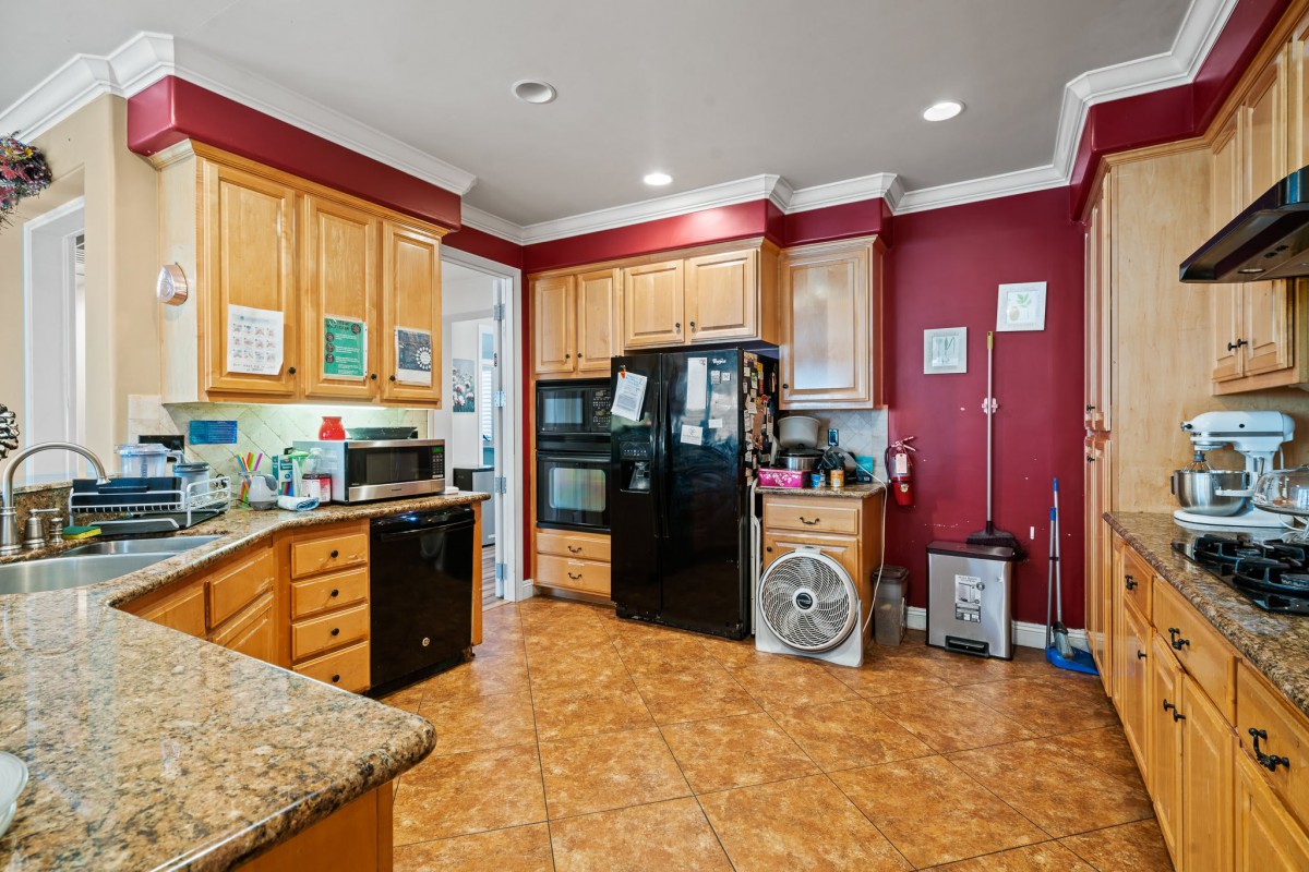 A spacious kitchen with red walls and wooden cabinets, featuring modern appliances including a black refrigerator and a microwave.