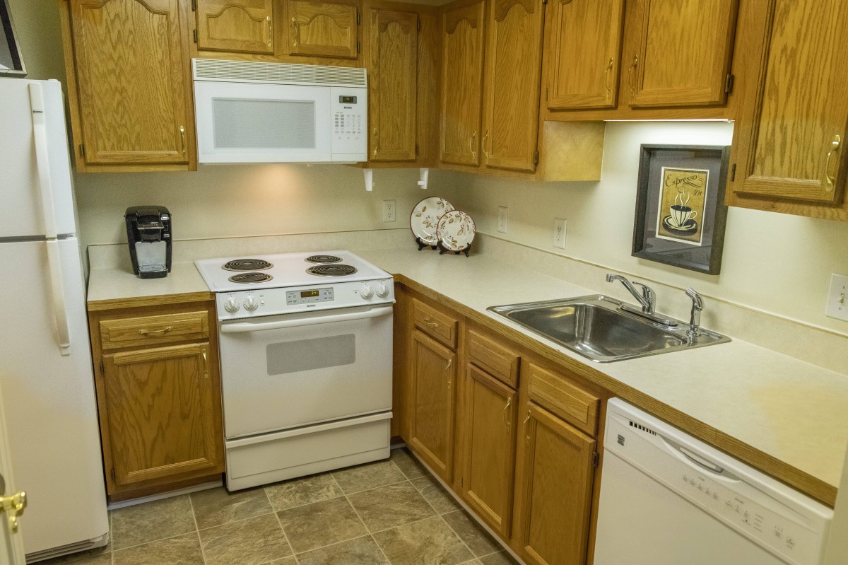 A cozy kitchen with wooden cabinets, featuring a stove, microwave, sink, and dishwasher.