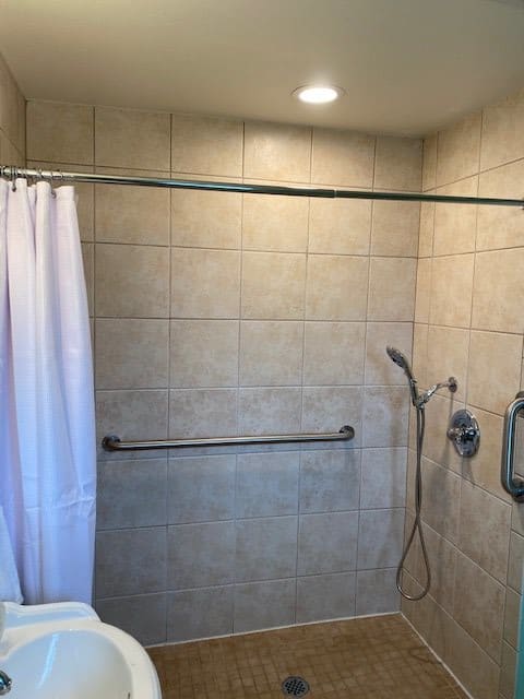 A bathroom shower area with beige tiles, a shower curtain, and a wall-mounted showerhead.