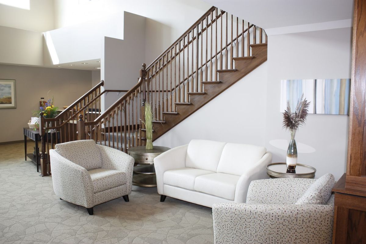 A modern living room with a white sofa, armchair, and a wooden staircase.