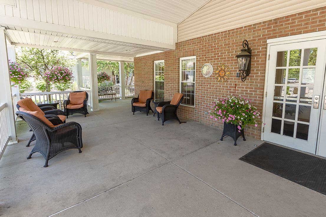 A cozy porch with wicker furniture and decorative plants against a brick wall.