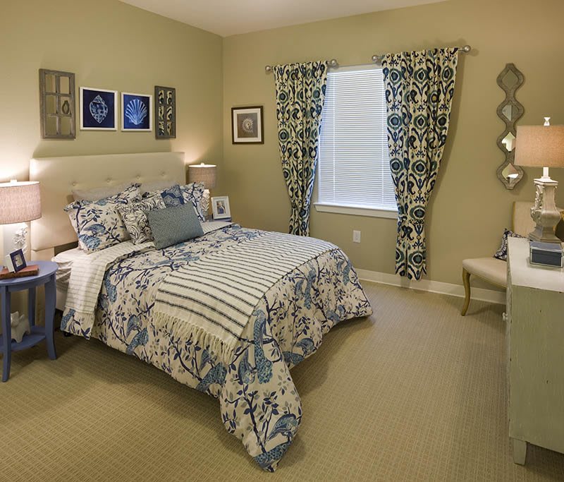 A cozy bedroom with patterned bedding and curtains, adorned with artwork and warm lighting.