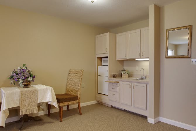 This image showcases a compact kitchen with white cabinets, a small dining set, and basic appliances.