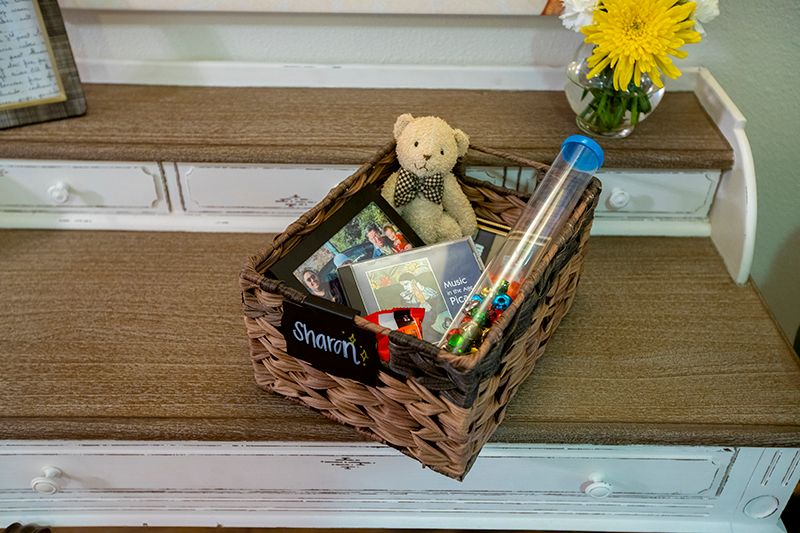 A basket on a staircase filled with a teddy bear, books, and toys alongside a vase of yellow flowers.